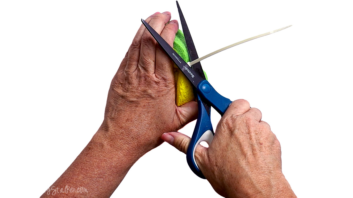 Hands using scissors to trim the excess end of a zip tie after securing sponge strips together to make a DIY sponge water bomb.