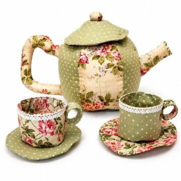 Handmade fabric tea set featuring a floral and polka dot teapot with matching teacups and saucers, finished with lace trim and soft stuffing.