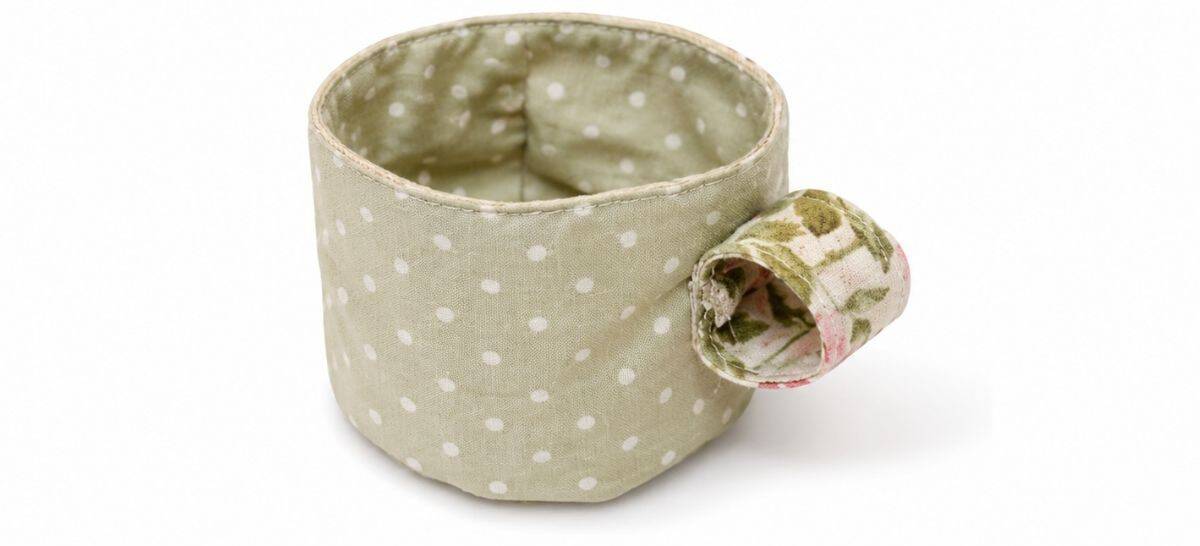 Soft fabric teacup with a floral-lined handle attached, featuring green polka dot fabric and stitched seams for a handmade toy tea set.
