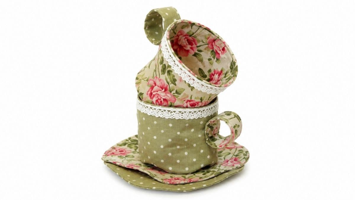 Floral and polka dot fabric teacups stacked on matching saucers, finished with delicate white lace trim as part of a handmade tea set.