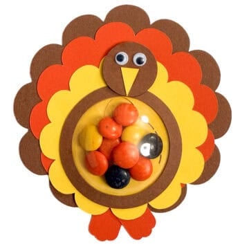 Paper turkey treat holder with layered brown, orange, and yellow feathers, googly eyes, and a clear dome filled with colorful candy.