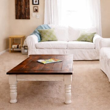 Refinished wooden coffee table with turned legs placed in a cozy living room, styled between two sofas with throw pillows and soft natural light.