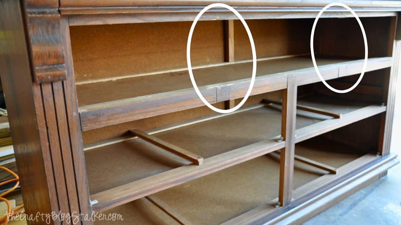 Wooden dresser frame with drawer sections removed, showing internal support braces partially cut out, highlighted with white ovals for modification reference.