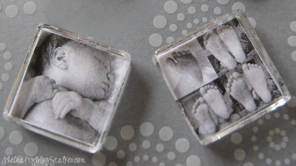 Two finished glass tile pendants with black-and-white baby photos sealed inside, one showing a sleeping baby and the other showing tiny feet.