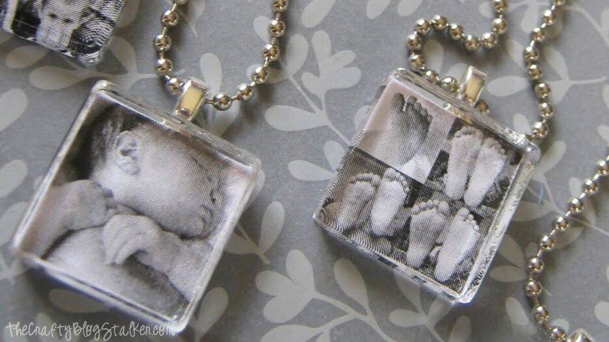 Two completed glass tile photo pendant necklaces with ball chains, featuring black and white images of a baby and baby feet.
