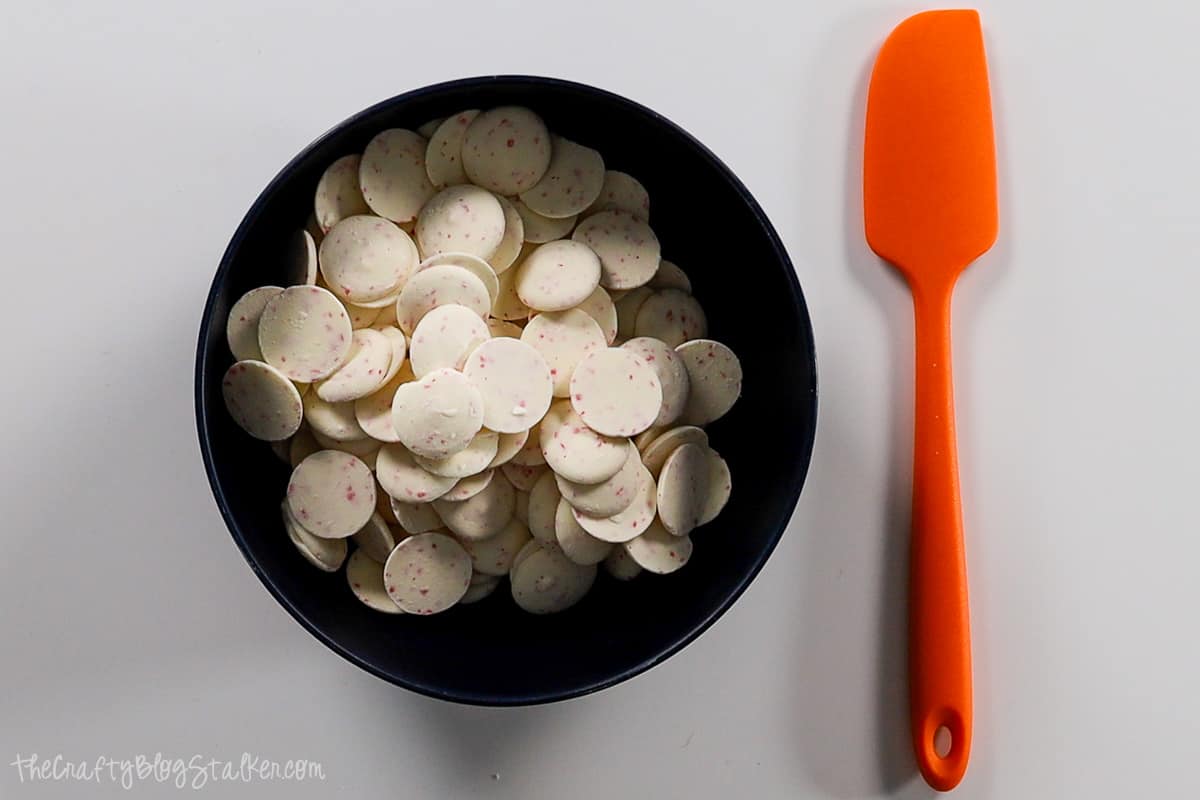 A bowl filled with peppermint chocolate pieces and an orange rubber spatula.