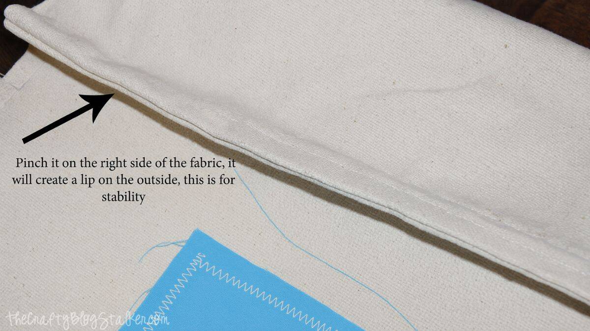 Close-up of folded canvas seam showing how to pinch the fabric to create a small outer lip for stability when finishing a tote bag edge.