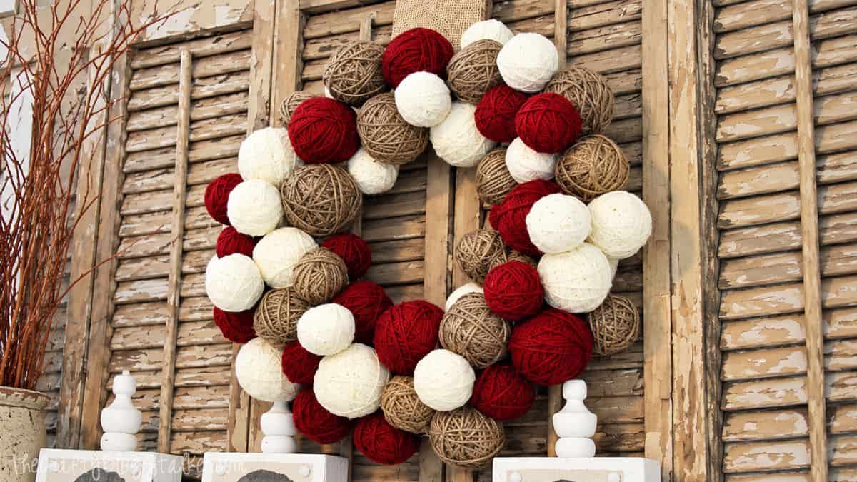 cheap way to make a yarn ball wreath Yarn ball wreath made with red, white, and tan yarn displayed against rustic wooden shutters.