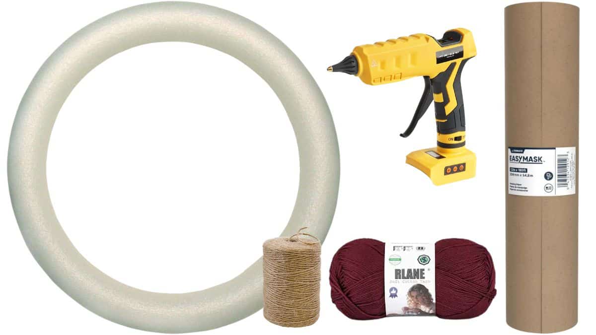 Supplies for a yarn ball wreath including a foam wreath form, hot glue gun, yarn, twine, masking paper, and cardboard tube.