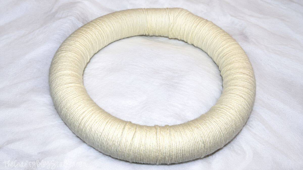 Foam wreath form completely wrapped in cream yarn as the base for a DIY yarn wreath.