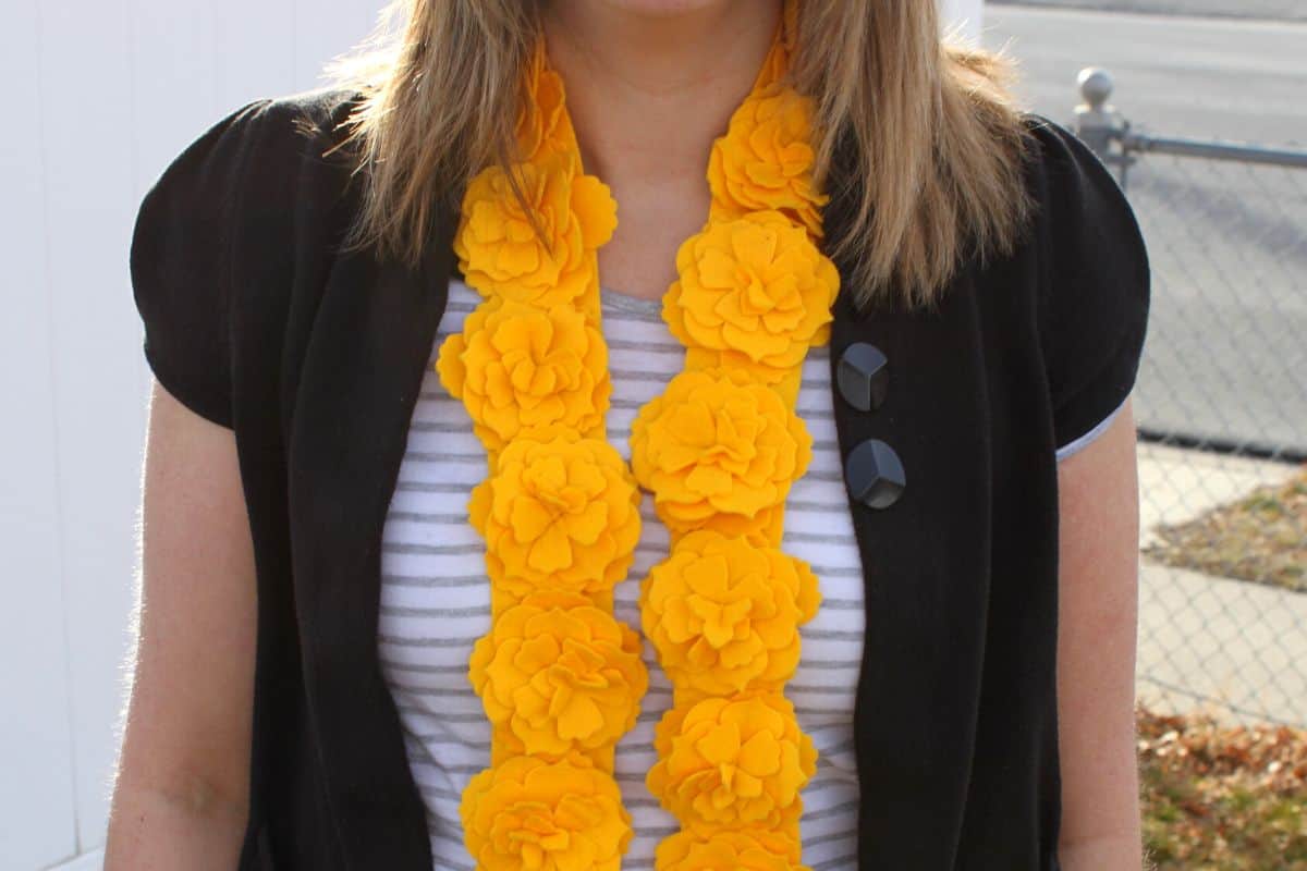 A woman wearing a yellow felt flower scarf hanging in front.
