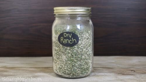 Glass mason jar filled with homemade dry ranch seasoning mix, labeled "Dry Ranch," on a wooden surface with a dark wood background.