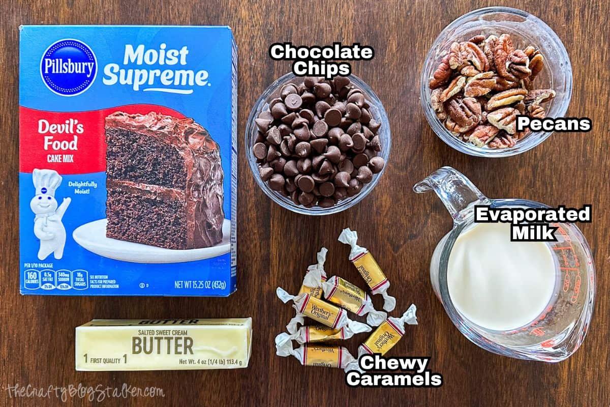 Ingredients for caramel turtle brownies: devil’s food cake mix, chocolate chips, pecans, butter, evaporated milk, and chewy caramels on a wooden surface.
