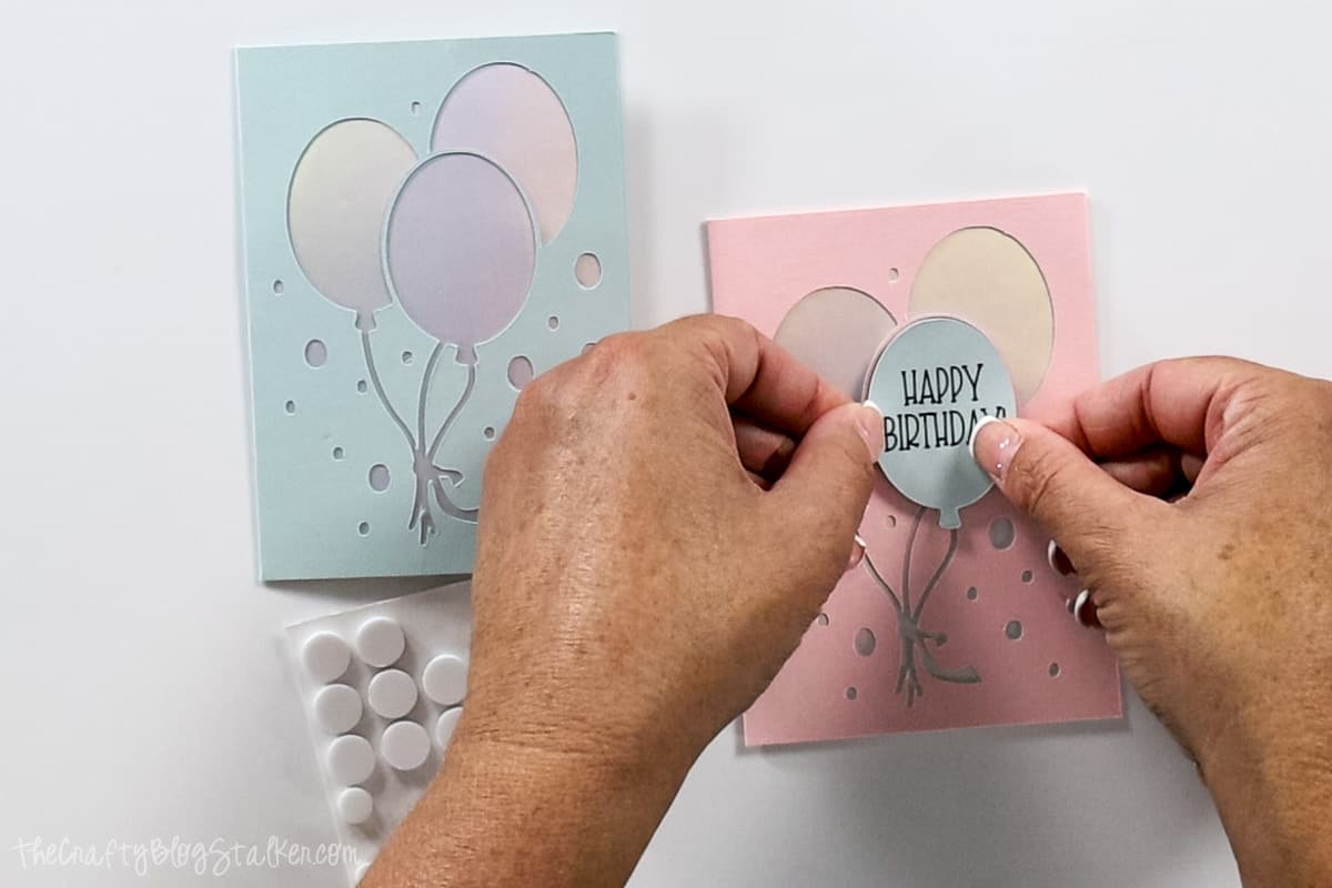 Adhering the 'Happy Birthday' Balloon on the card with adhesive foam dots.