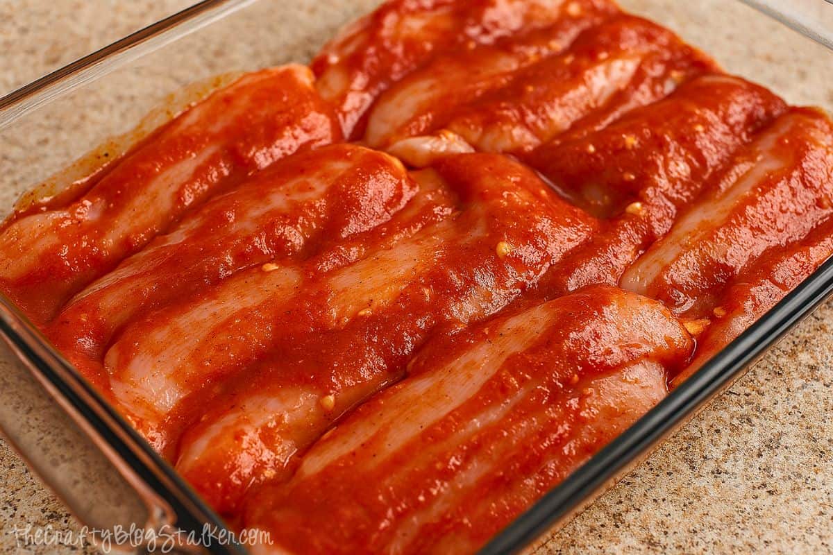 Raw chicken breasts arranged in a glass baking dish, coated in a thick layer of homemade BBQ marinade.
