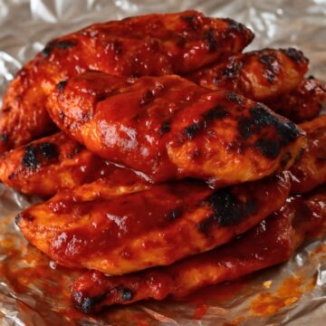Grilled chicken tenders coated in a thick, glossy layer of homemade BBQ sauce, served on a sheet of aluminum foil.