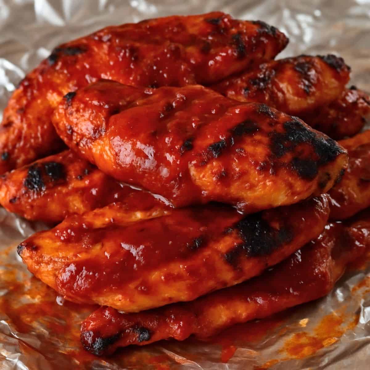 Grilled chicken tenders coated in a thick, glossy layer of homemade BBQ sauce, served on a sheet of aluminum foil.