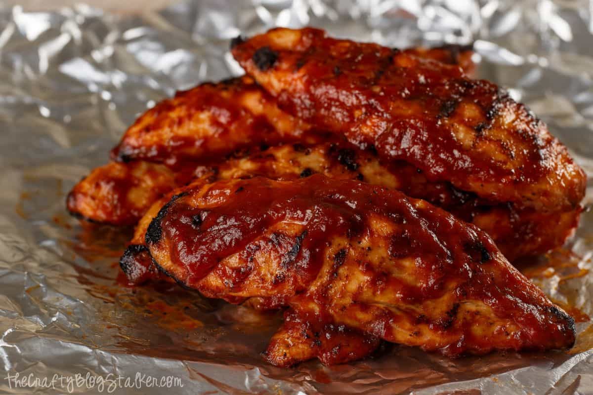 Grilled chicken breasts coated in thick, glossy BBQ sauce, served hot on a sheet of crinkled aluminum foil.