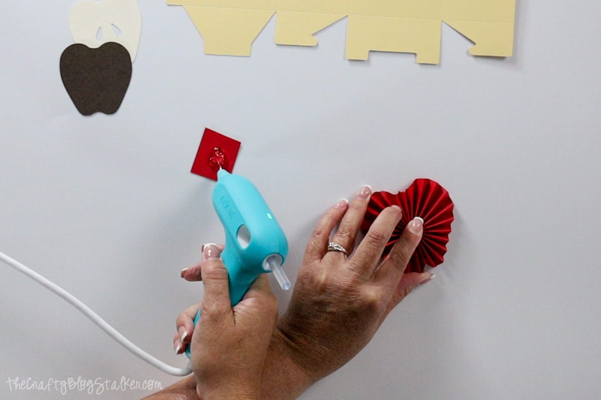 Applying a glob of hot glue onto a red square of cardstock.