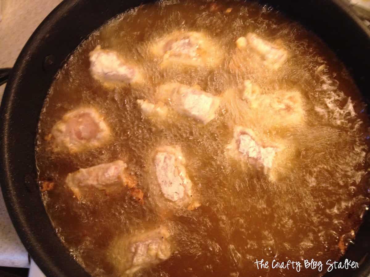 Chicken nuggets frying in a skillet with hot oil.