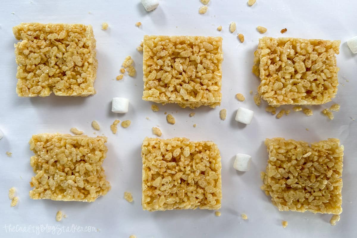 Six Rice Krispy Treats with crumbs and marshmallows around.
