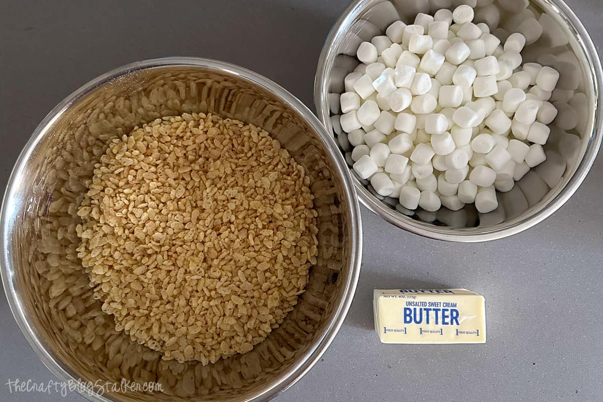 A bowl of Rice Kripsie cereal, a bowl of marshmallows, and a cube of butter.