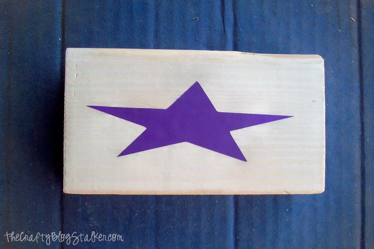 a vinyl star placed on a piece of wood to be used ads a stencil