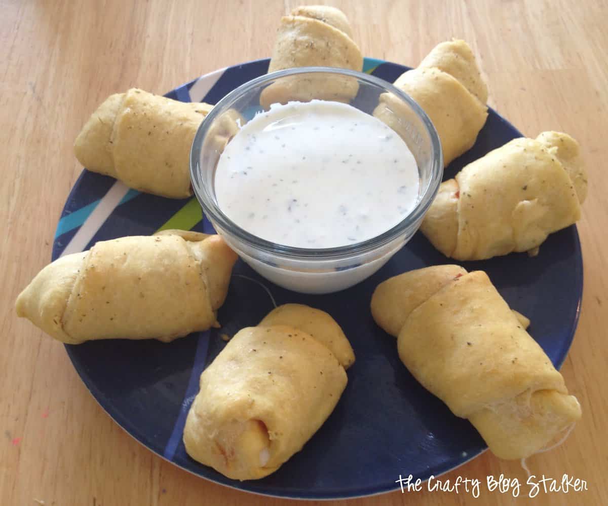 Pepperoni String Cheese Roll Ups on a plate with a bowl of ranch.