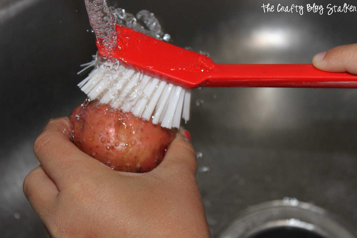 image of washing a potato with a red vegetable brush