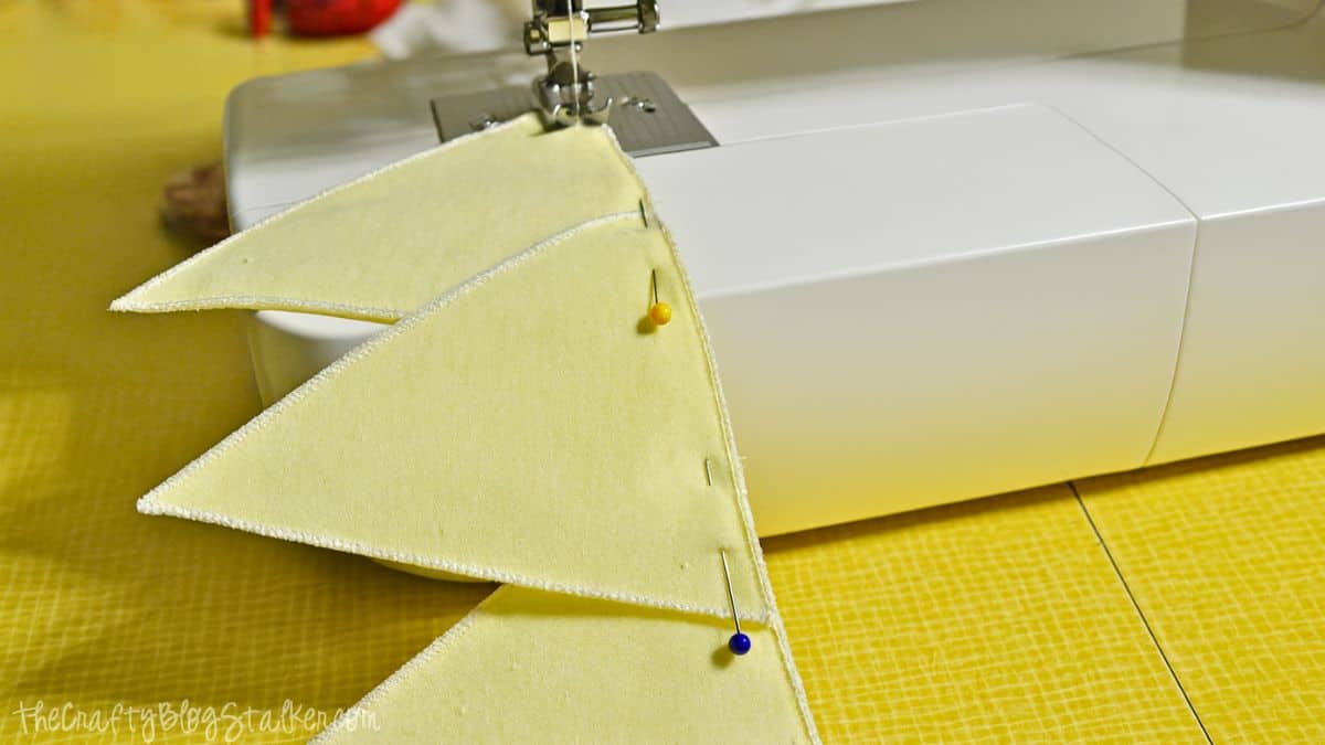 Yellow fabric triangles pinned together and being stitched with a sewing machine on a yellow table.