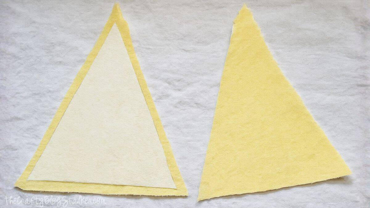 Two yellow fabric triangles, one layered with interfacing, laid flat on a white surface for a sewing project.