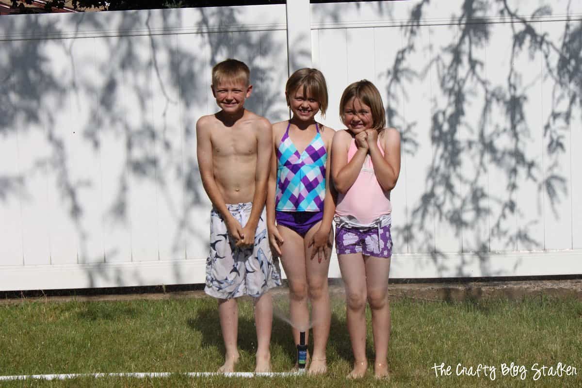 three kids standing in the sprinkler