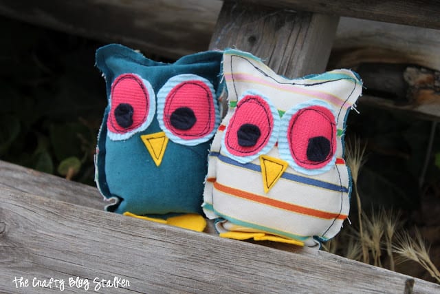 Two stuffed owls sitting on a piece of wood.