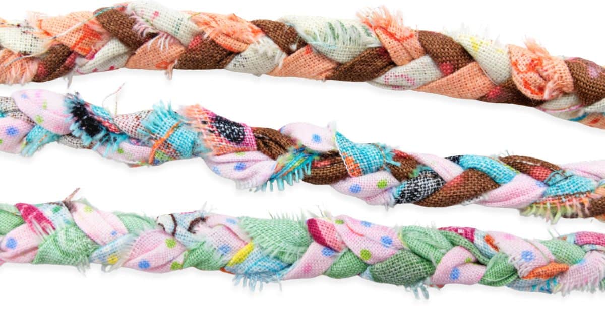 Three colorful braided fabric strips in various pastel and earthy tones, each with frayed edges, showcasing a DIY textile crafting technique.
