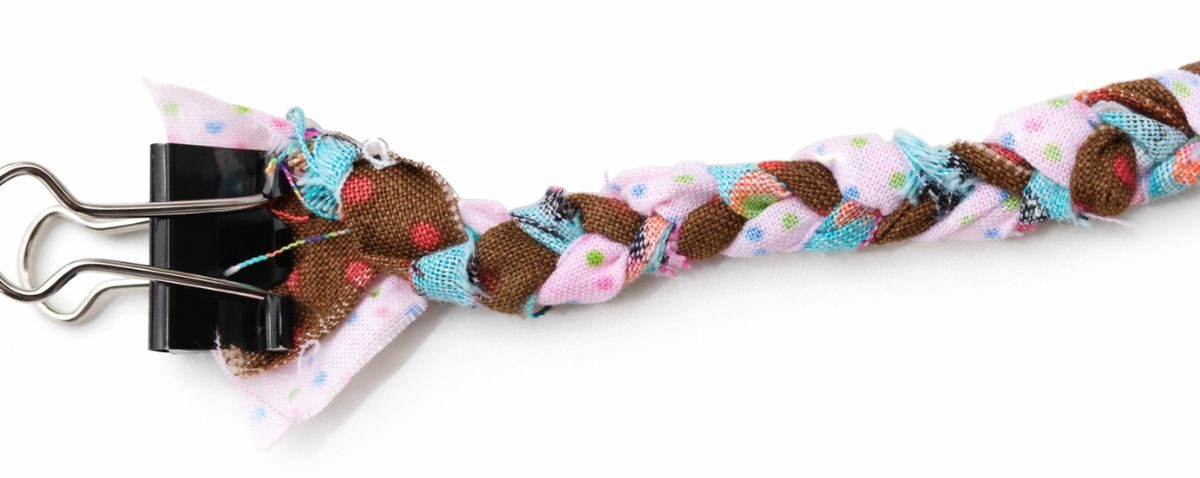 A close-up of braided fabric strips in pink, brown, and blue polka dot patterns, secured at one end with a black binder clip, perfect for DIY and crafting projects.