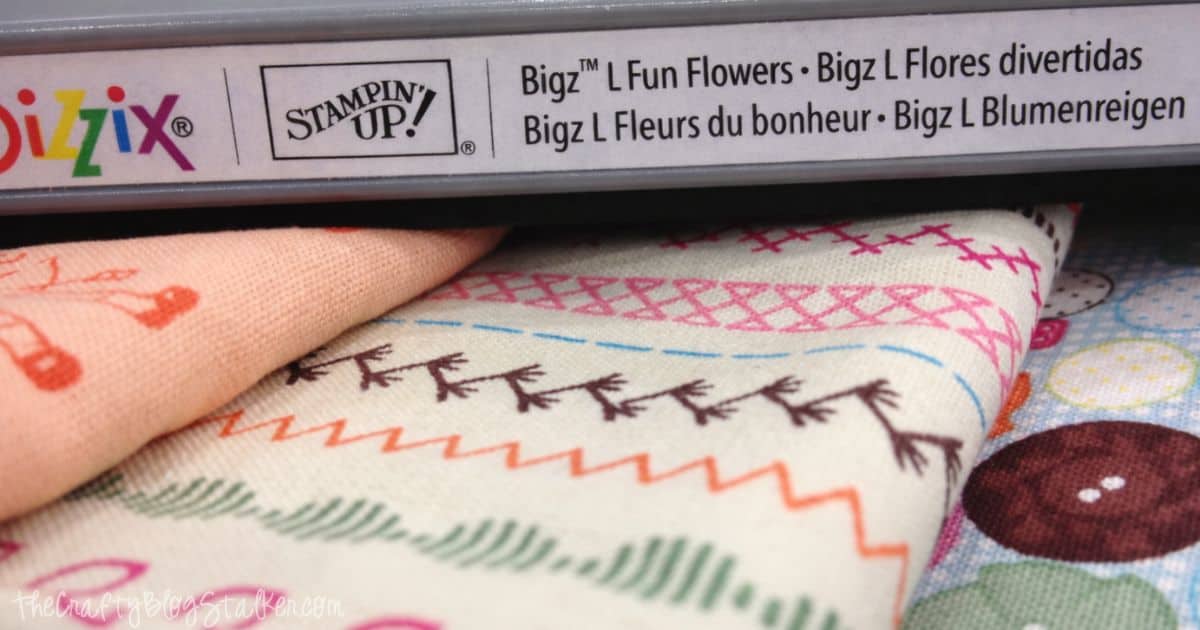 Close-up of Sizzix Bigz L Fun Flowers die by Stampin' Up! alongside colorful, patterned fabric, showcasing crafting tools and materials for fabric die-cutting projects.