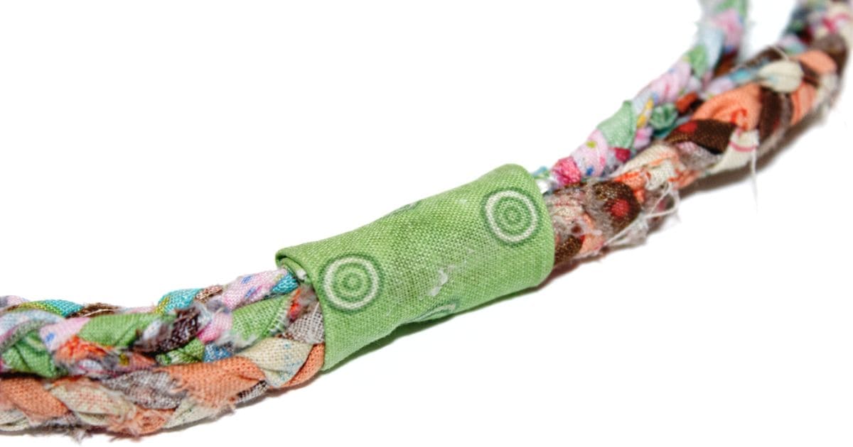 Close-up of a colorful braided fabric with a green fabric strip wrapped and glued securely around the ends, providing a neat finish for a handmade project.