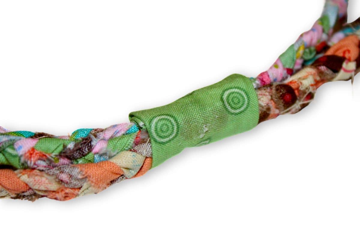 Close-up of a colorful braided fabric with a green fabric strip wrapped and glued securely around the ends, providing a neat finish for a handmade project.