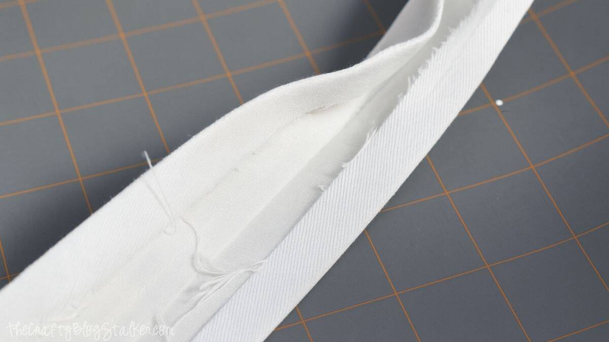 Close-up of a white fabric strap folded lengthwise and pressed with seams visible, prepared for sewing handles onto a handmade tote bag.