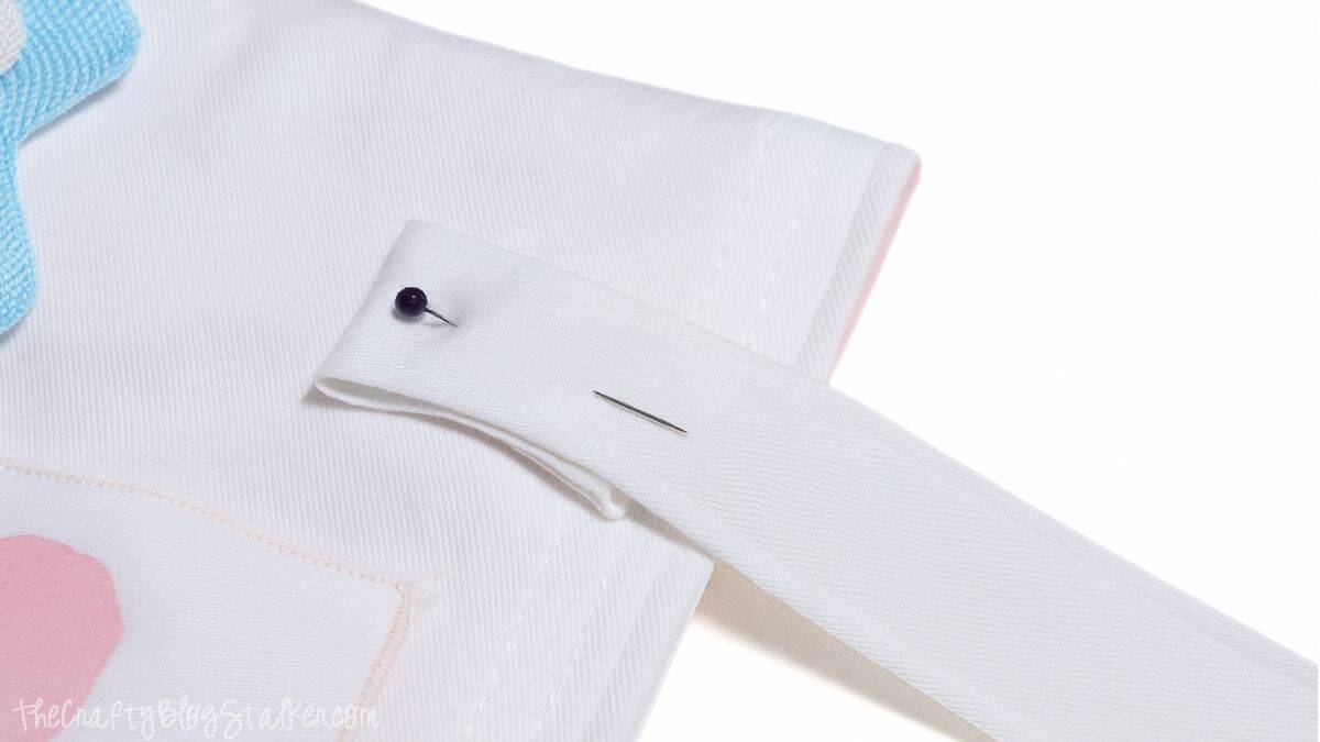 White fabric strap pinned to the top edge of a sewn tote bag, showing how to attach handles before stitching them in place.