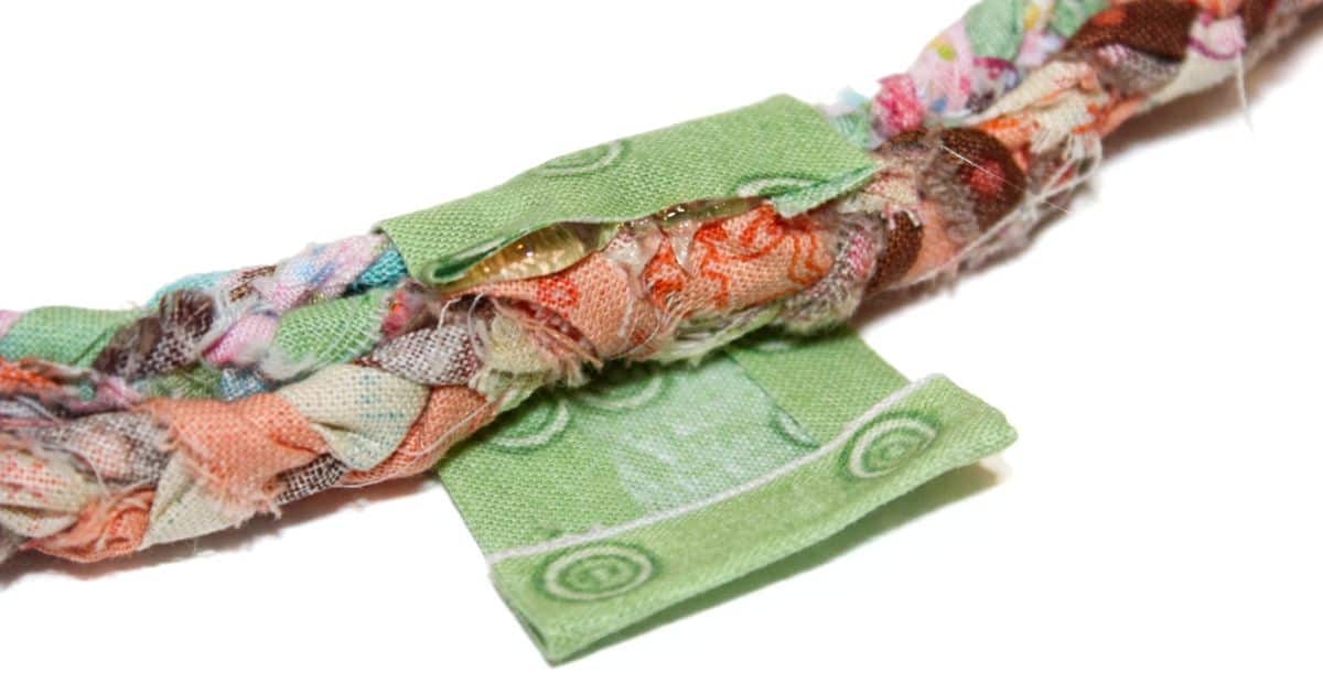 Close-up of colorful braided fabric with a green fabric piece being glued on top, showing how to cover and secure the braided ends for a clean, finished look.