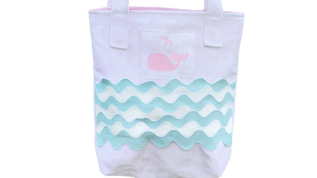 White toddler tote bag with blue and white ric rac waves and a pink whale applique, finished with sturdy fabric straps for carrying.