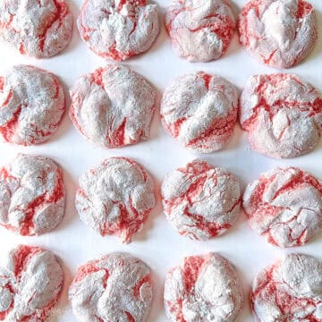 Pink lemonade crinkle cookies baked with cracked tops and a powdered sugar coating, arranged closely together on a flat surface.