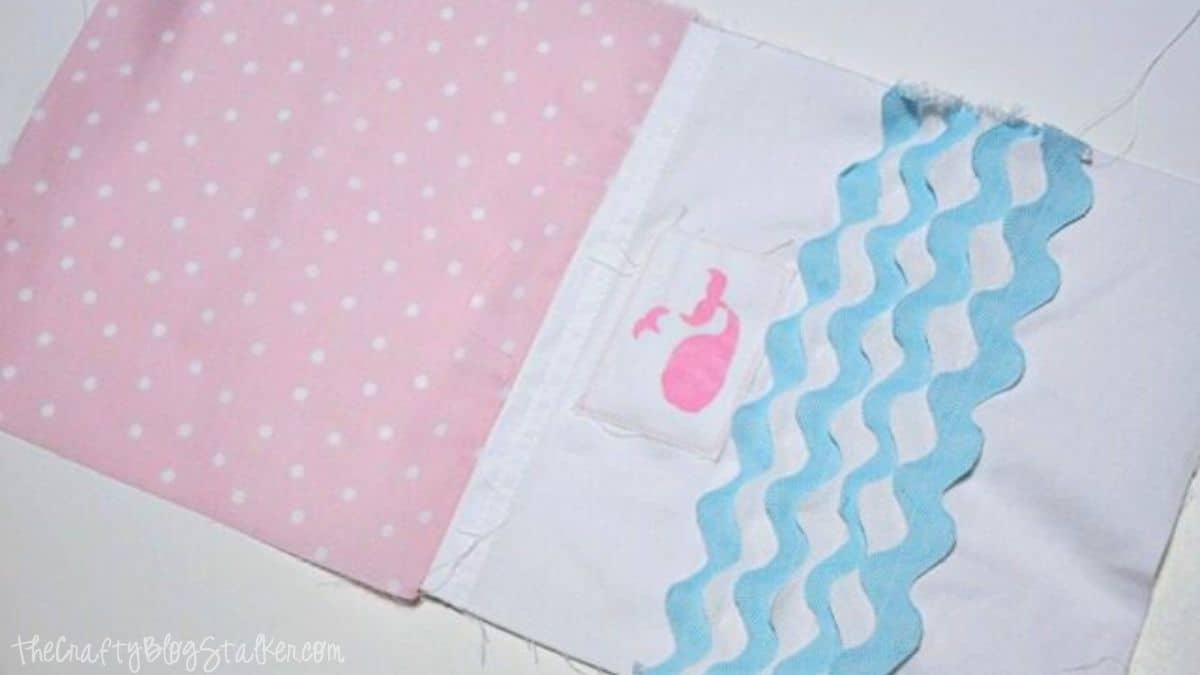 Pink polka dot fabric sewn to a white fabric panel with blue ric-rac waves and a small pink whale patch, showing the front and lining of a tote bag in progress.