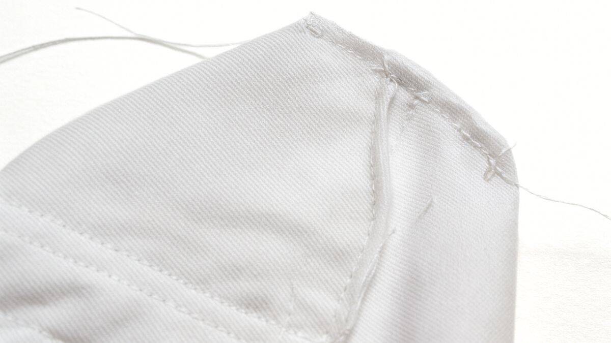 Close-up of white fabric showing a sewn gusset corner, demonstrating how to create depth and shape in the bottom of a tote bag.