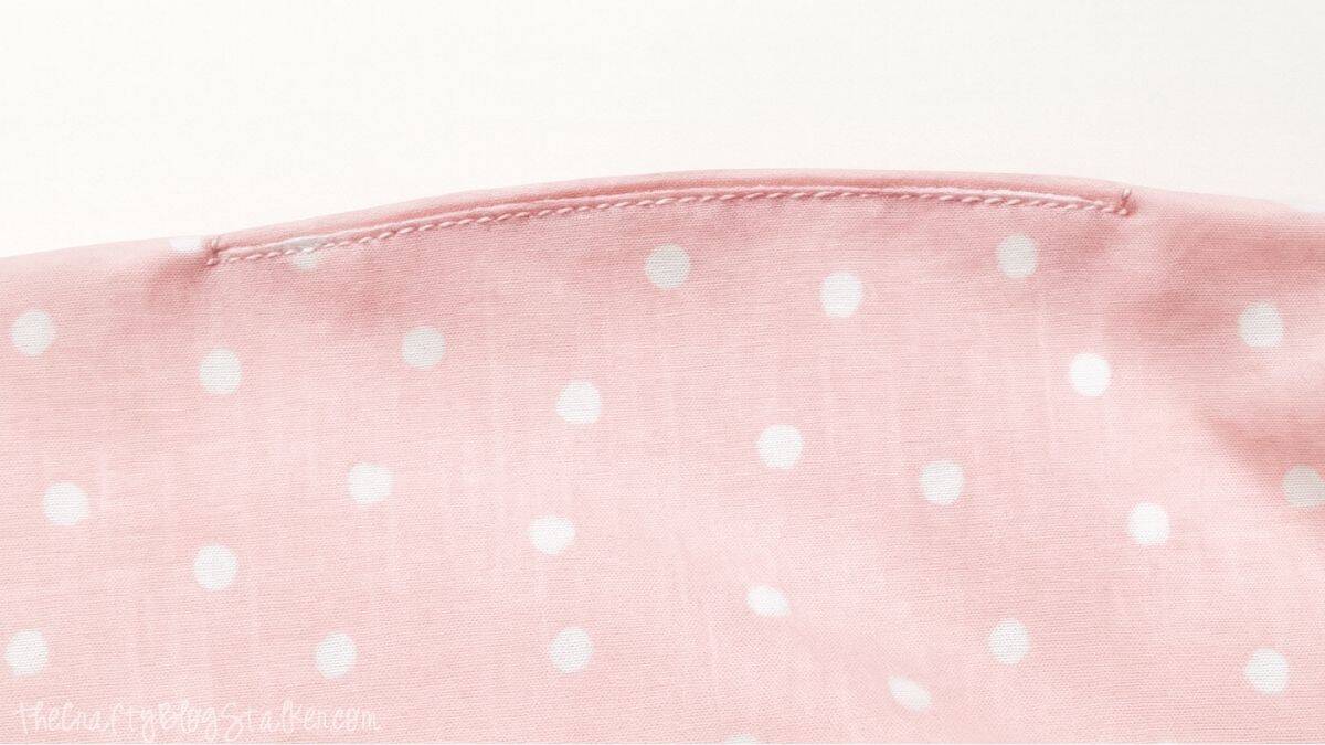 Close-up of pink polka dot fabric with a seam stitched closed, showing the finishing step of sewing a tote bag lining hole shut.