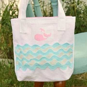 Handmade toddler tote bag with blue and white ric rac waves and a pink whale applique, displayed outdoors on a chair.