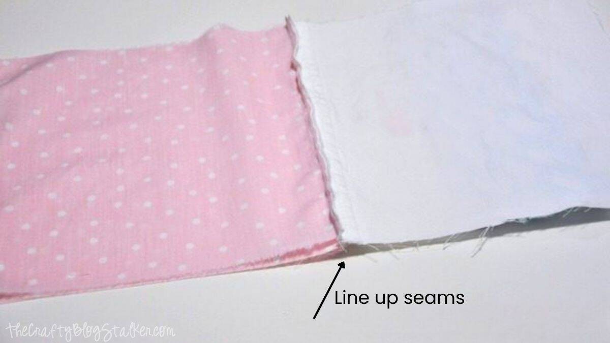 Pink polka dot fabric and white fabric placed side by side with seams aligned, showing the step to line up seams before sewing tote bag pieces together.