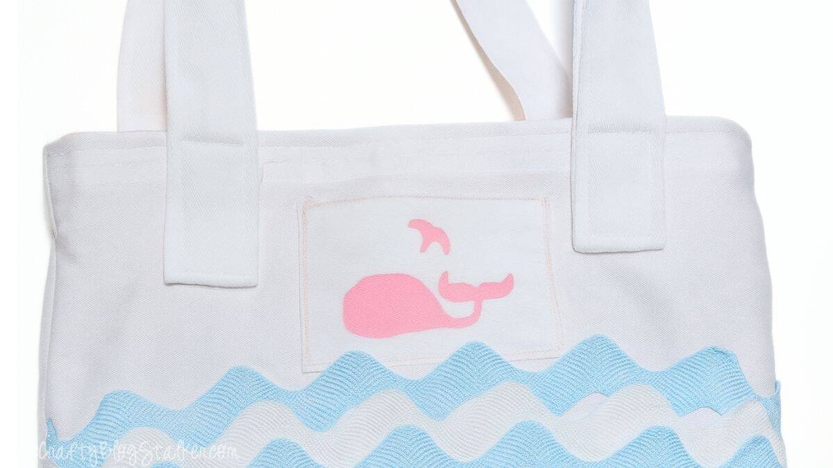 White tote bag with blue ric rac waves, a pink whale applique, and securely sewn white fabric straps attached at the top.