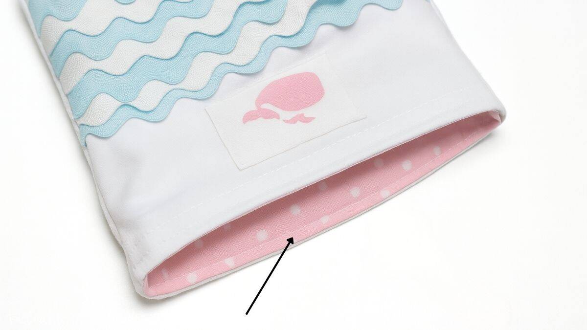 Close-up of a handmade tote bag with ric rac wave trim, a pink whale applique, and pink polka dot lining, showing top stitching around the bag's opening.